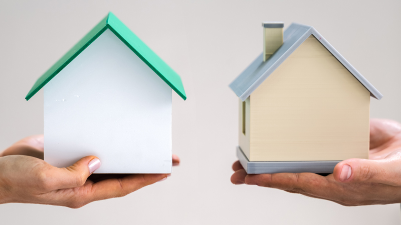 Duas mãos seguram duas casas de cartão, frente a frente